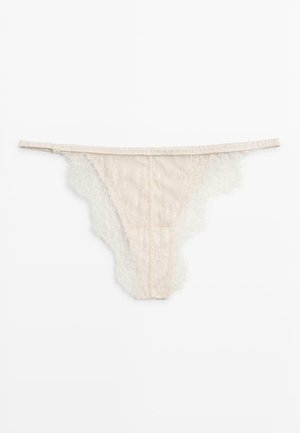 Beżowe koronkowe stringi z falistymi krawędziami i cienkim paskiem na talii, położone płasko na białym tle.