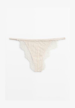 Beige Spitzen-String mit wellenförmigen Kanten und dünnem Taillenbund, flach auf weißem Hintergrund liegend.