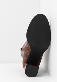 Botte texturée marron avec une fermeture éclair sur le côté, dotée d'une semelle en caoutchouc noire et d'un talon bloc. La tige présente un motif peau de serpent.