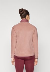 Giacca in pile rosa chiaro con colletto alto, maniche lunghe e una texture liscia. L'orlo e i polsini hanno un bordo coordinato.