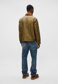 Καφέ ανοιχτό, λείο μπουφάν με γιακά, σε συνδυασμό με μπλε τζιν παντελόνι. Καφέ υποδήματα με υβριδική σόλα ολοκληρώνουν την εμφάνιση.