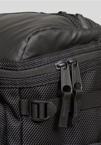 Mustakankaan tekstuurisuudella varustettu reput, jonka kulmassa on kaksoissalpa sekä säädettävä sivuhihna muovipokalla.