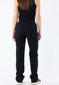 Pantaloni sportivi neri con cintura elastica, vestibilità dritta e una tasca posteriore. Il modello indossa una canotta nera e scarpe casual.