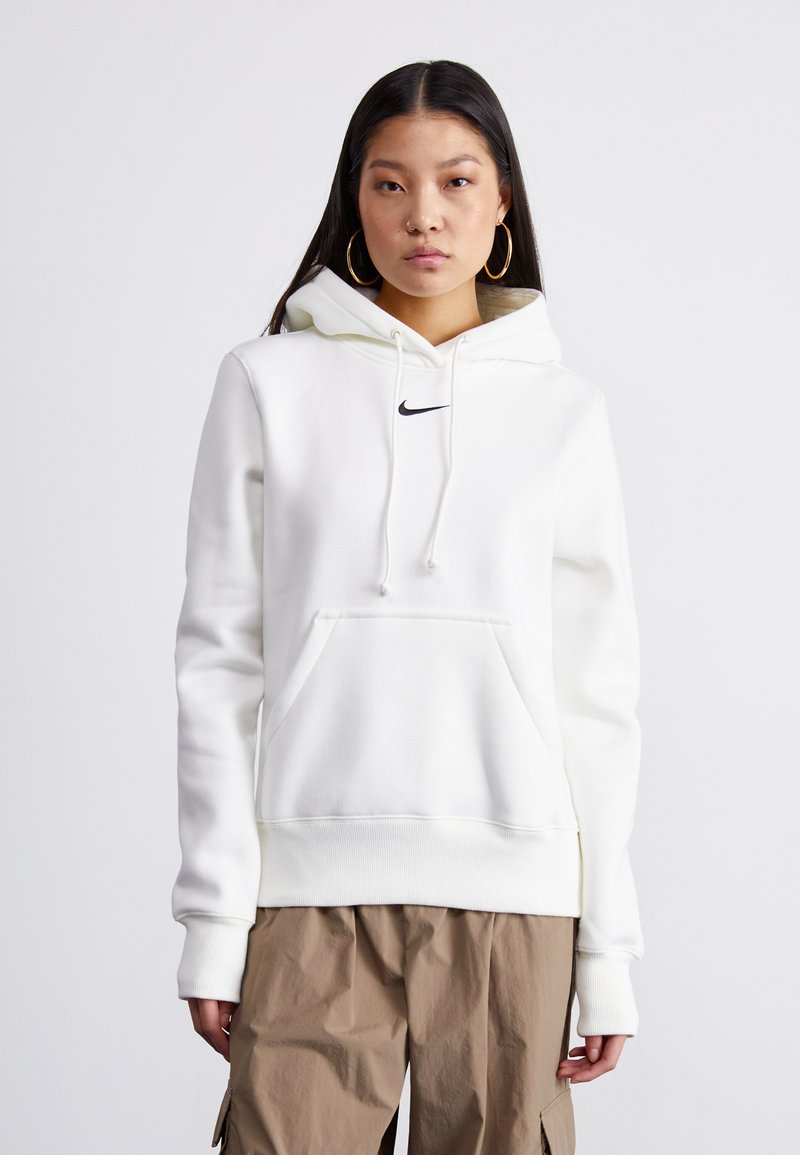Haut à capuche Nike blanc avec une poche frontale, un cordon de serrage, et un petit logo noir sur la poitrine, fabriqué en tissu doux et texturé.