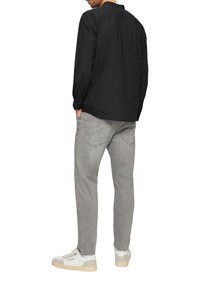 Chemise noire à manches longues en tissu texturé, jean gris à coupe ample et baskets blanches avec des accents beige. Design minimaliste, look décontracté.