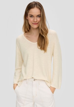 Hellbeige Langarmshirt mit Rundhalsausschnitt, weicher Textur und lässiger Passform, kombiniert mit hochgeschnittenen weißen Jeans.