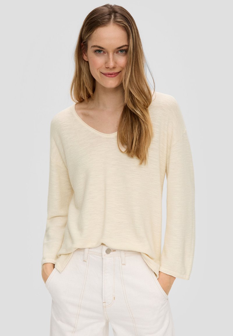 Hellbeige Langarmshirt mit Rundhalsausschnitt, weicher Textur und lässiger Passform, kombiniert mit hochgeschnittenen weißen Jeans.