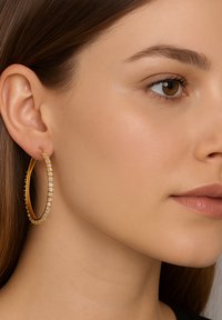 Gold hoop earring featuring a smooth finish and clear gemstone accents along the outer edge. Oval shape complements the ear.
