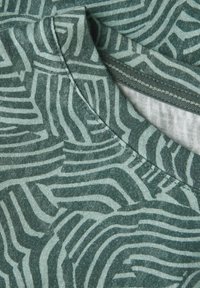 Tissu vert à motifs avec des lignes ondulées dans différentes nuances de vert. Gros plan sur la surface texturée et le détail du col rond.