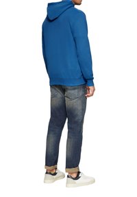 Blauwe hoodie met een trekkoordkap, gecombineerd met vervaagde spijkerbroek en lichtgekleurde sneakers met een donkere accent. Casual pasvorm.