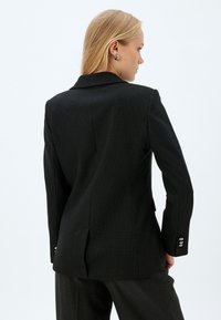 Zwarte pinstripe blazer met een getailleerd ontwerp, ingeplante revers, enkele achterventilatie en zilveren knopen op de mouwen. Gekleed textuur.