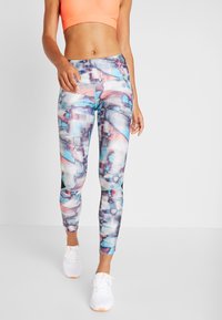 Leggings dengan pola cat air abstrak berwarna biru, merah muda, dan abu-abu. Terbuat dari kain elastis dengan desain pas. Dipadukan dengan sepatu sneakers putih.