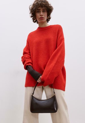 Maglione rosso oversize in maglia con scollo a girocollo, abbinato a pantaloni larghi color avorio e una piccola borsa nera in pelle.