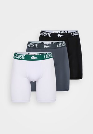 Tres pares de boxers para hombre: blancos, grises y negros. Cada uno presenta cinturillas distintas con el logotipo de Lacoste en colores contrastantes.