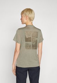 Alyvos žalios spalvos marškinėliai trumpomis rankovėmis, su keturių skyrių abstrakčiu spaudu nuolaidžiais tonais nugaroje. Minkšta tekstūra, laisvas kirpimas.