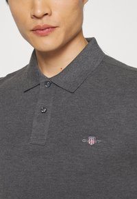 Mørkegrå polo-shirt i blødt materiale med struktureret krave og to-knap placket; har lille logo på brystet.