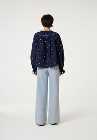 Navyblaues Hemd mit weißen gestickten Akzenten, übergroßen Ärmeln und gefälteltem Rückendetail, kombiniert mit hellblauen, weit geschnittenen Jeans.