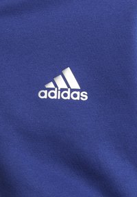 Sininen puuvillakangas, jossa on näkyvä valkoinen Adidas-logo kolmannella raidalla, sileä pinta ja rento muotoilu, joka sopii urheiluvaatteisiin.