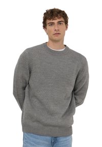 Maglione grigio a maglia con scollatura rotonda e polsini a coste. Il tessuto appare morbido con una finitura strutturata, abbinato a jeans in denim blu chiaro.