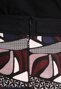 Czarna góra z tkaniny z wielokolorowym abstrakcyjnym nadrukiem w odcieniach czerwieni, niebieskiego i bieli; posiada widoczny zamek błyskawiczny i ozdobne detale.