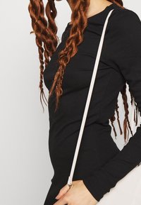 Svart ribbad långärmad topp med figurnära silhuett, i kombination med en vit axelväska med kviltad design och justerbar rem.