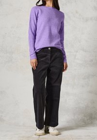 Maglione viola a maglia con maniche lunghe, abbinato a pantaloni larghi in velluto a coste neri e sneakers bianche con accenti neri.