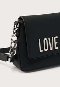 Μαύρο τσαντάκι χιαστί από ψεύτικο δέρμα με ασημένια αλυσίδα, διακοσμημένο με την επιγραφή «LOVE» σε μεταλλικά γράμματα στο εμπρόσθιο καπάκι.