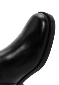 Bottine en cuir noir avec une finition lisse, bout rond et semelle noire basse et robuste. Présente des coutures discrètes le long du bord.