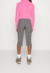 Sudadera de forro polar en un vibrante color rosa, combinada con pantalones cortos gris hasta la rodilla que cuentan con bolsillos de carga y detalles de cremallera, llevados con zapatos de senderismo beige.