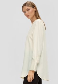 Langärmlige, cremefarbene Bluse aus leichtem Stoff mit V-Ausschnitt und abgerundetem Saum. Verfügt über Knopfmanschetten und ein minimalistisches Design.