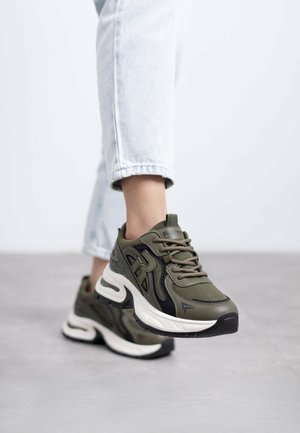 Zapatillas deportivas en verde oliva, confeccionadas con material de malla y sintético, con una suela blanca gruesa y detalles en negro, diseñadas para ofrecer comodidad y soporte.