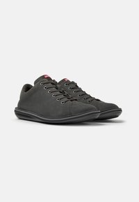Sneakers scamosciati grigio scuro con una texture liscia, suola in gomma, lacci piatti e un piccolo tag con logo sulla linguetta. Design minimale.