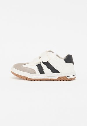 Hvite og grå sneakers med svarte striper, overdel i semsket skinn og syntetiske materialer, borrelåsstropper, gummisåle og "Luchi"-logo på hælen.