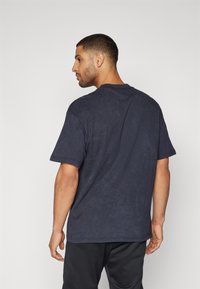 Mørkeblå t-shirt med korte ærmer lavet af blødt stof med en afslappet pasform, der har en rund halsudskæring og en subtil tekstur.