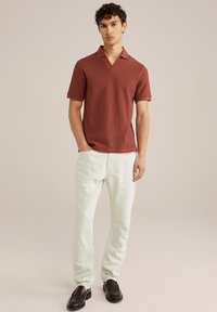 Short-sleeve, rust-colored polo shirt with a textured pattern and a V-neck, paired with light-colored linen pants and black loafers.