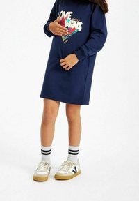Granatowa sukienka dresowa z kolorową, cekinową grafiką z napisem "MIŁOŚĆ zawsze ZWYCIĘŻA". Dodatkowo w połączeniu z kremowymi trampkami i pasiastymi skarpetkami.