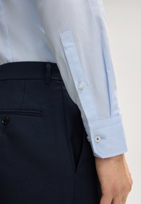 Hellblau gemusterte Hemd aus strukturiertem Stoff, mit Knopfmanschetten, kombiniert mit dunkelblauen Hosen mit klarer Linienführung und seitlichen Taschen.