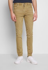 Kakigröna slim-fit jeans i bomullsmix, med framfickor, subtila slitningar och dragkedja. Kombinerat med vita sneakers.