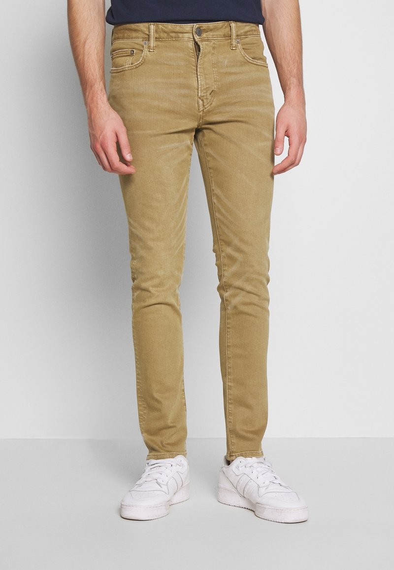 Kakigröna slim-fit jeans i bomullsmix, med framfickor, subtila slitningar och dragkedja. Kombinerat med vita sneakers.