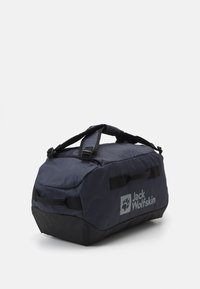Borsa da viaggio resistente in blu navy con fondo nero, maniglie superiori, tracolla regolabile e logo riflettente Jack Wolfskin.