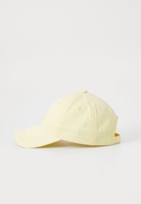 Casquette de baseball jaune avec une visière incurvée, texture en tissu et strap ajustable à l'arrière. Dispose de trous de ventilation et d'une couronne arrondie.