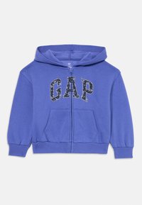 Haut à capuche zippé bleu avec une poche avant, arborant le logo "GAP" dans un motif floral sombre. Fabriqué en tissu doux avec des poignets élastiques.