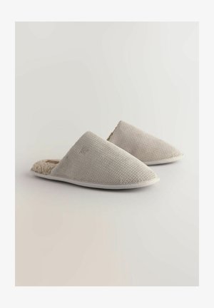 Texturirane bež copate s softim, puhast notranjim podlogom in belim gumijastim podplatom, ki imajo odprt hrbet in koničast dizajn prstov.