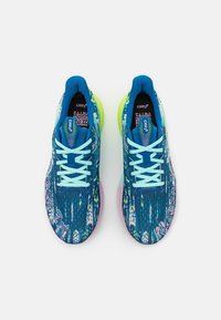 Løbesko har en blå mønstret tekstiloverdel, lyseblå snørebånd, grønne accenter og en pink mellemsål. Designet til atletisk ydeevne.