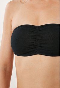 Melnā bezplecu bikini augšdaļa ar gludu tekstūru, ar savilkumu centrā un izliekta dekoltē. Piemērota peldkostīmiem.