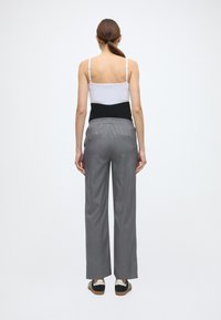 Μπλούζα σε στρώσεις ασπρόμαυρη με λεπτές τιράντες, συνδυασμένη με γκρι, άνετο, πλισέ παντελόνι και μαύρα αθλητικά παπούτσια καθημερινής χρήσης. Απλός σχεδιασμός.