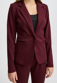 Blazer ajustado burdeos hecho de material suave, con solapa de muesca, cierre de un solo botón y bolsillos laterales.