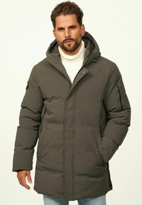 Gepolsterte, kapuzenjacke in Dunkelgrün. Verfügt über Seitentaschen, eine Reißverschlusstasche am Arm und einen strukturierten Strickkragen unterhalb des Reißverschlusses.