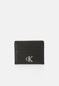 Tarjetero de cuero negro con superficie texturizada, cuatro ranuras para tarjetas y un logotipo plateado de "CK" en la parte frontal. Diseño delgado.
