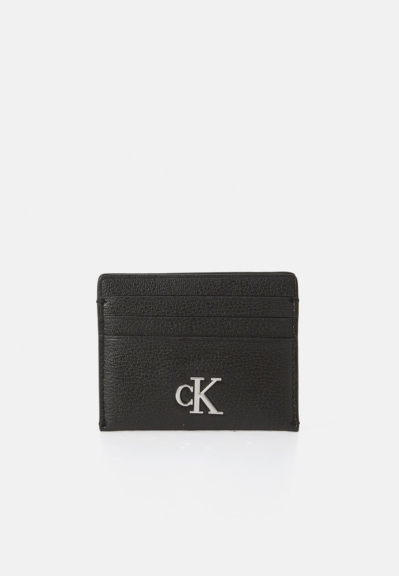 Tarjetero de cuero negro con superficie texturizada, cuatro ranuras para tarjetas y un logotipo plateado de "CK" en la parte frontal. Diseño delgado.